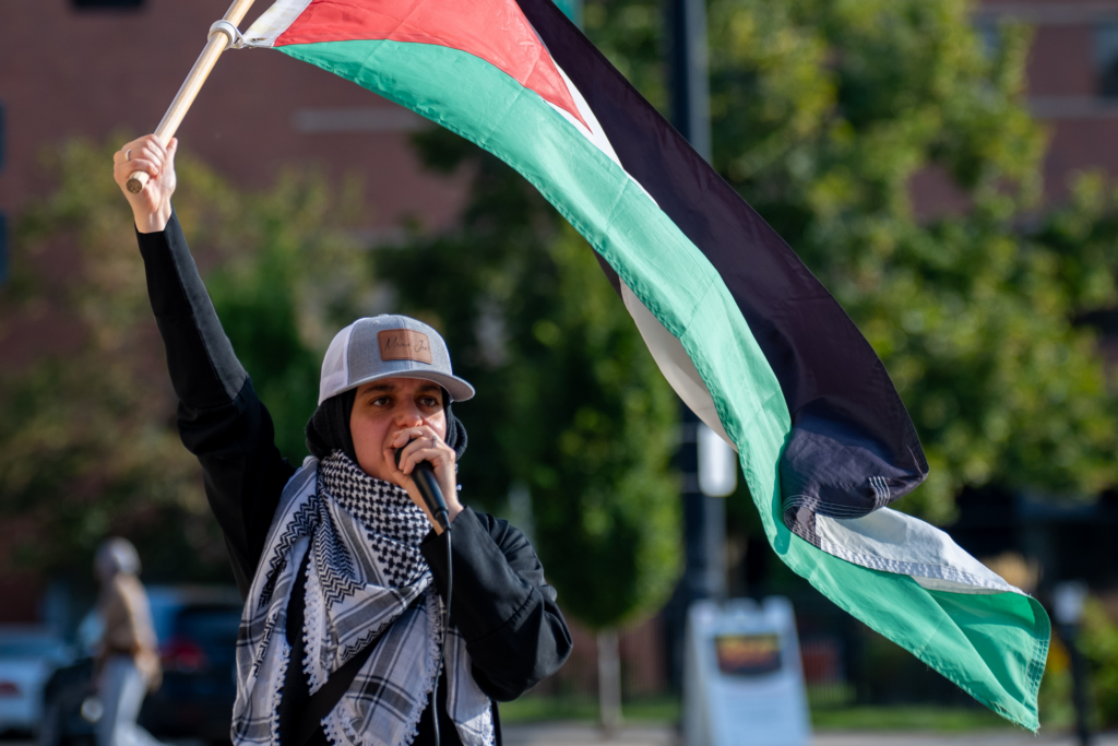 Photo of Dua Aldasouqi at a CU MAC event holding a microphone and Palestinian flag.